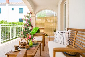 Un balcon avec un banc en bois, une table avec une tasse et un vase de fleurs, et un canapé blanc avec des coussins à rayures.