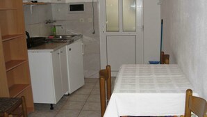 A compact kitchen with white cabinets, a sink, and a small countertop. There is a dining table with chairs and a window with frosted glass. - Apartments Pinija - Two Bedroom Apartment with Terrace (Supetar)