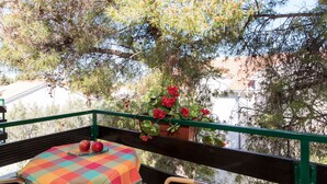 A balcony with a table set for two, a chair, and a potted plant with red flowers. - Apartments Pinija - Two Bedroom Apartment with Terrace (Supetar)