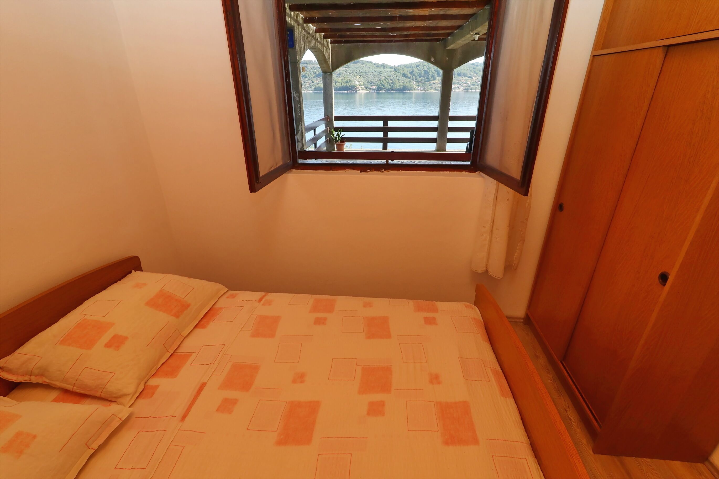 Une chambre à coucher avec un lit, une fenêtre donnant sur un pont et des collines, et une armoire en bois.