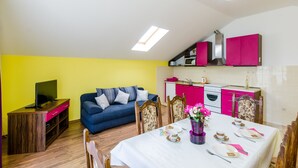 A compact living space with a dining area, kitchenette, and a TV on a wooden stand. - Apartments Mali Paradiso - Two Bedroom Apartment with Balcony and Pool View (Mlini)