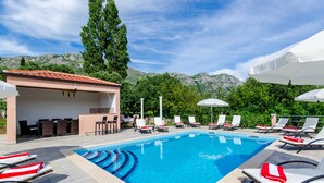 A swimming pool with lounge chairs and umbrellas, surrounded by greenery and mountains. - Apartments Mali Paradiso - Two Bedroom Apartment with Balcony and Pool View (Mlini)