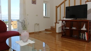 Una sala de estar con una mesa de centro de vidrio, un sofá rojo, una estantería de madera y un televisor sobre un mueble de madera.