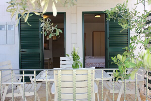 A patio with white furniture and green shutters, a white table with a vase of flowers, and a view into the interior of the building.
