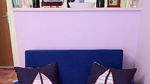 A blue sofa with two pillows featuring sailboat designs, positioned in front of a window with decorative bottles and a framed picture. - Apartments Vera - Comfort One-Bedroom Apartment with Terrace and Sea View (Irena) (Okuklje)