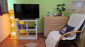 A living room with a TV on a stand, a bookshelf, a wooden cabinet, a rocking chair, and a floor lamp. - Apartments Vera - Comfort One-Bedroom Apartment with Terrace and Sea View (Irena) (Okuklje)