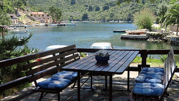 A wooden deck with a table and benches overlooking a lake with boats and houses in the background. - Apartments Vera - Comfort One-Bedroom Apartment with Terrace and Sea View (Irena) (Okuklje)