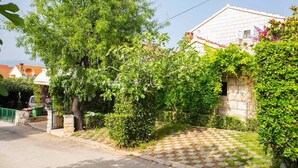 A residential area with a paved driveway, a large tree, and a house with a tiled roof. - Apartments Roda - Comfort One Bedroom Apartment with Terrace (Supetar)