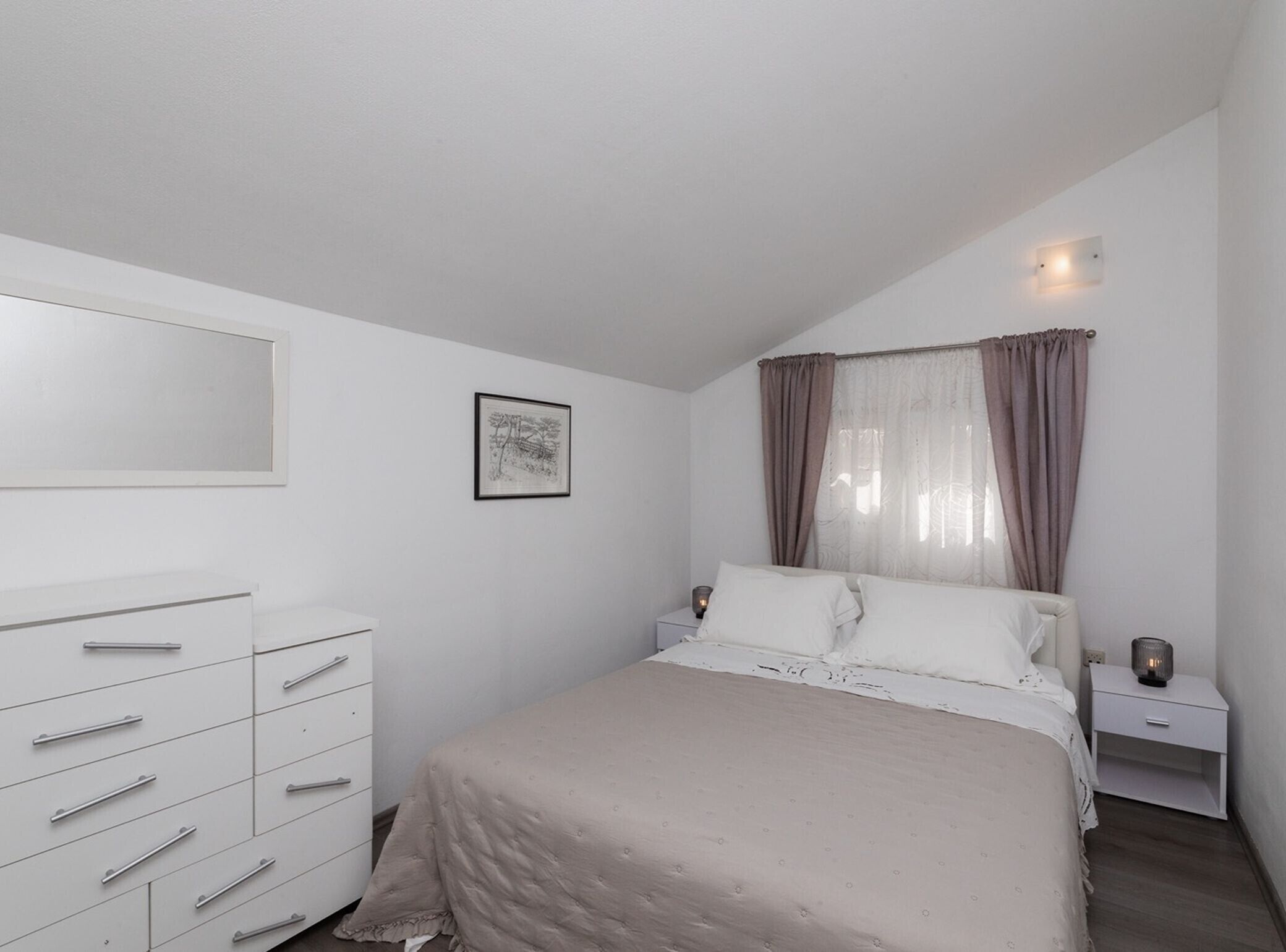 Ein Schlafzimmer mit Bett, Schminktisch, Nachttisch, Wandlampe und einem gerahmten Bild.