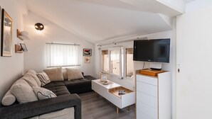A modern living room with a sectional sofa, a flat-screen TV, a white cabinet, and a window with blinds. - Apartments Roda - Comfort One Bedroom Apartment with Terrace (Supetar)