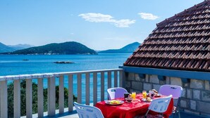 Une table dressée sur un balcon donnant sur la mer, avec des montagnes qui se dessinent à l’horizon.