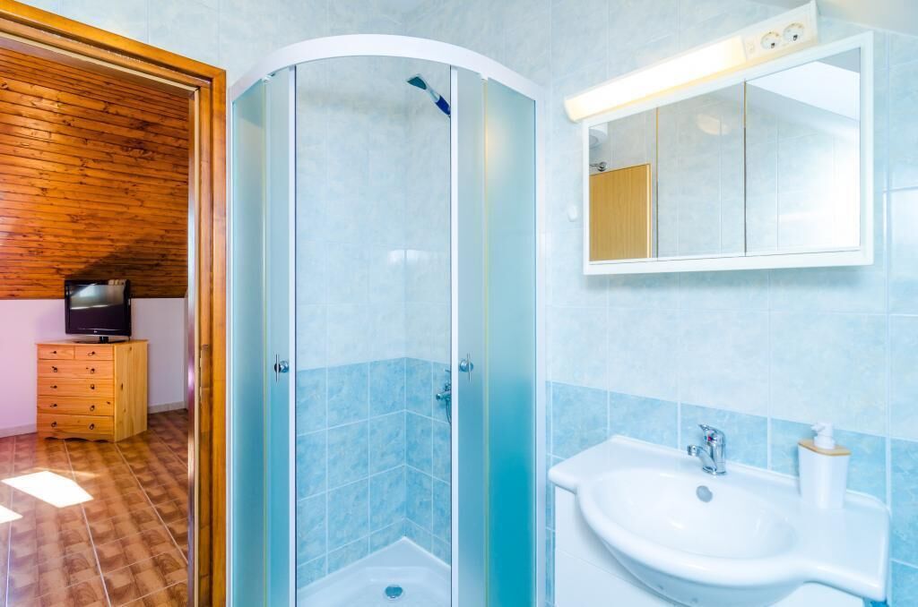 Une salle de bain avec une douche à parois de verre, un lavabo et un meuble en bois intégrant un téléviseur.