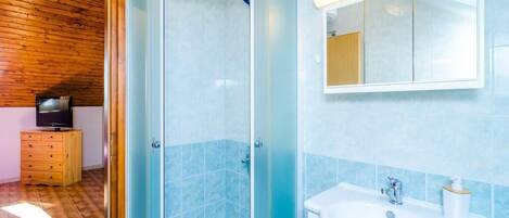 Une salle de bain avec une douche à parois de verre, un lavabo et un meuble en bois intégrant un téléviseur.