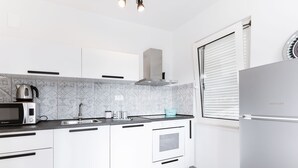 Eine moderne Küche mit weißen Schränken, einer eingebauten Mikrowelle, einem Wasserkocher und einem Kühlschrank.