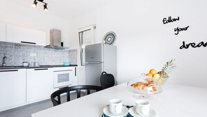 Eine moderne Küche mit weißen Schränken, einem Edelstahlkühlschrank und einem Essbereich mit weißem Tisch und Stühlen.