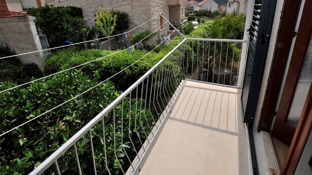 A balcony with a metal railing overlooking a garden and neighboring buildings.