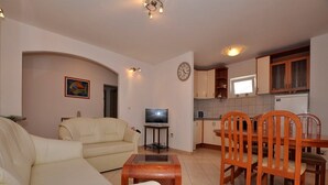A living room with a sofa, a television, and a dining area with wooden chairs and a table.