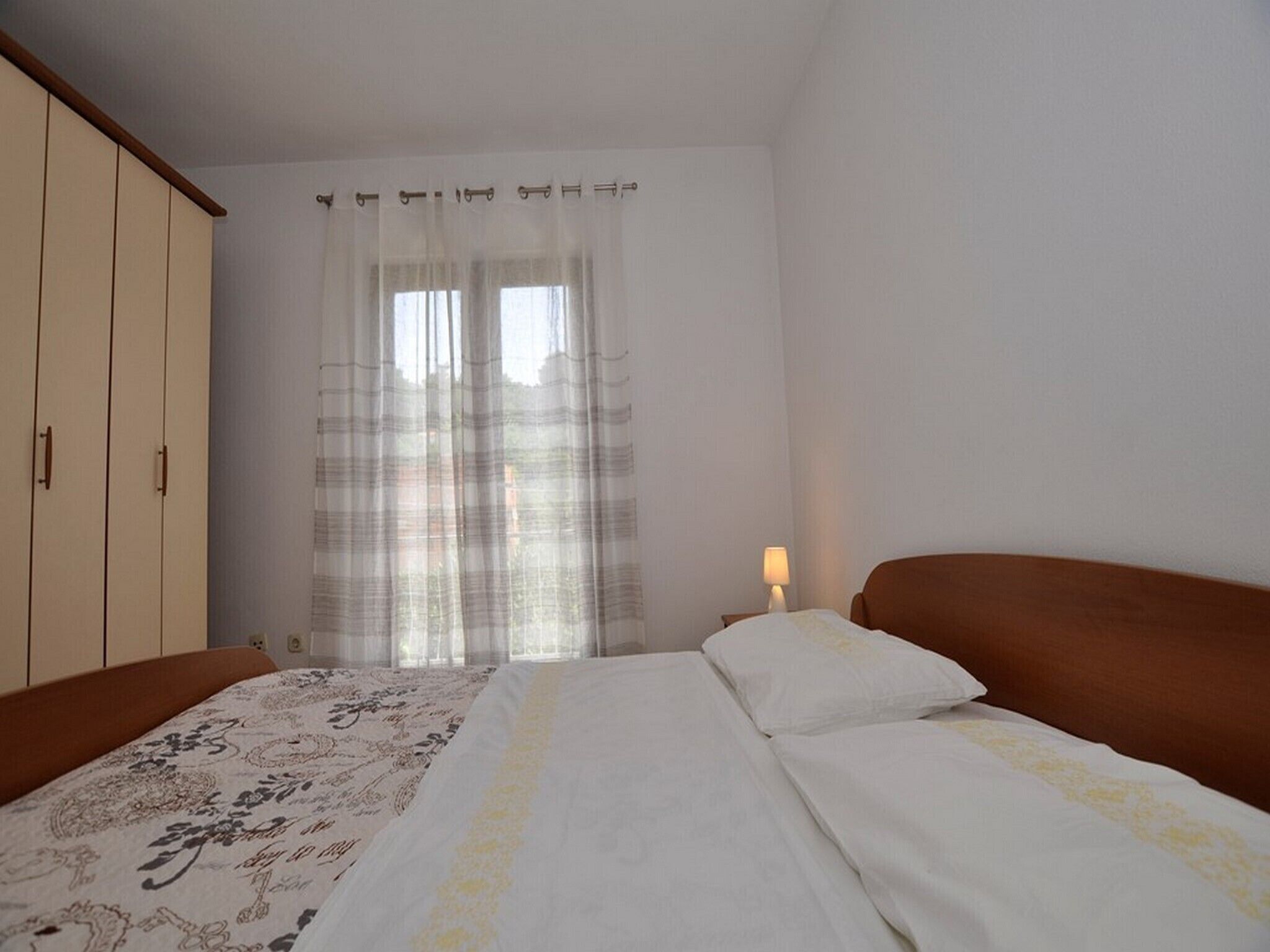 A bedroom with a bed, a wardrobe, and a window with curtains.