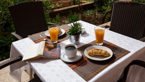 Une table dressée à l’extérieur, avec un livre, une tasse de café, un croissant et deux verres de jus d’orange.