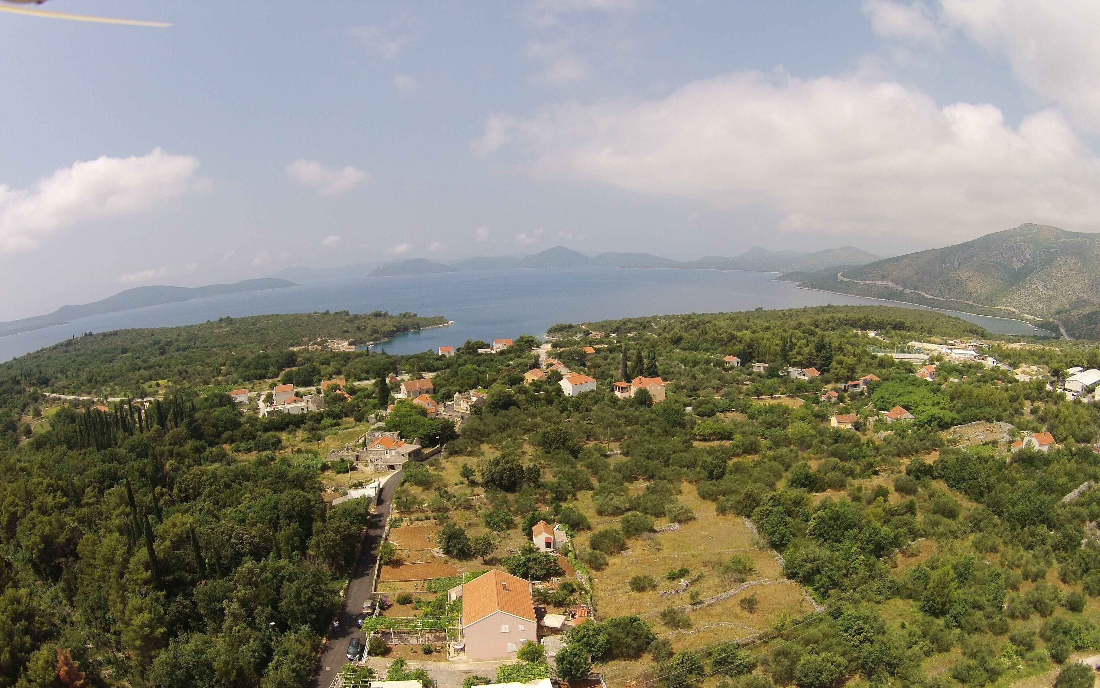 A coastal village with houses surrounded by greenery and a view of the sea and mountains.