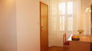 A small room with a wooden door, a table with a basket of fruit, and a vase with flowers. - Room Lazareti - Double Room with Shared Terrace (Dubrovnik)
