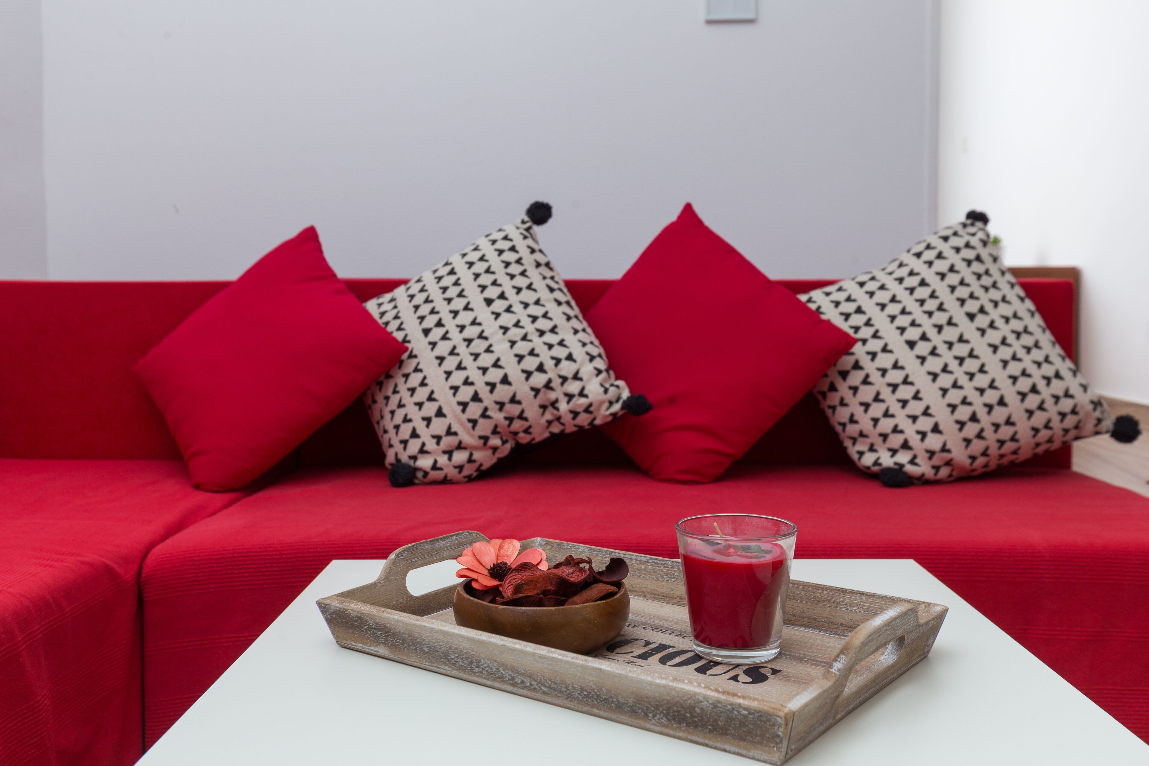 A red sofa with patterned cushions and a tray with a drink and decorative items on a white table.