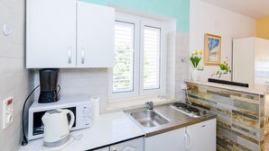Een moderne keuken met witte kastjes, een magnetron, een waterkoker, een spoelbak en een raam met jaloezieën.