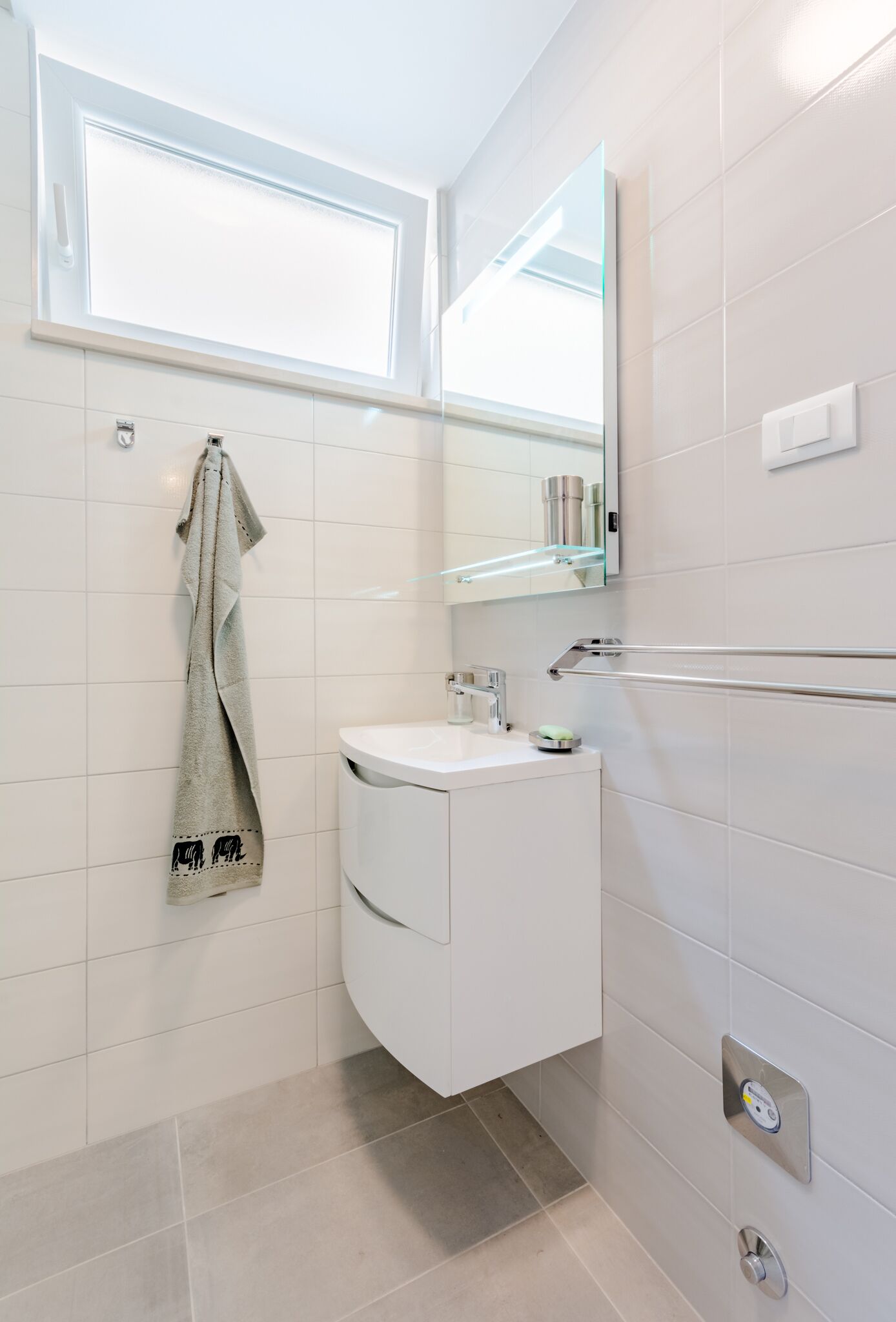 A modern bathroom with a white vanity, a towel hanging on the wall, a glass shower enclosure, and a mirror above the sink.