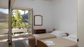 Ein Hotelzimmer mit zwei Betten, einem kleinen Tisch, einem Spiegel und einer Schiebetür zu einem Außenbereich mit Pflanzen.