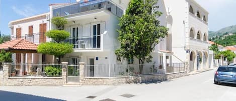 A two-story building with balconies, a stone wall, and a parked car.