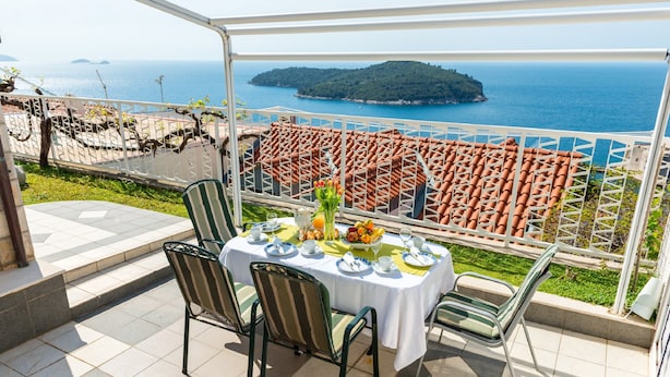 Eine Terrasse mit Esstisch, Stühlen und Blick auf das Meer und eine entfernte Insel.