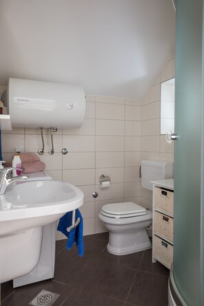 Un bagno con lavandino bianco, WC e termoconvettore a parete. Sono presenti cesti e un porta asciugamani.