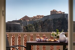 Un balcone con un tavolo apparecchiato per la colazione, con vista su un'antica muratura in pietra e edifici con tetti in tegole.