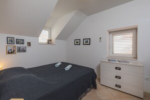 A bedroom with a bed, a dresser, a window with blinds, and framed pictures on the wall.