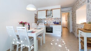 A modern kitchen with white cabinets, a tiled backsplash, and a dining area with white chairs and a table.