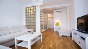 A modern living room with a white sofa, a white coffee table, a TV stand, and a wooden floor.
