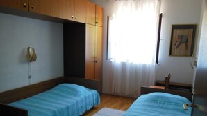 A bedroom with two single beds, wooden wardrobe, a small table, and a window with curtains. - Apartment Sea Side - Two Bedroom Apartment with Sea View Terrace (ST) (Postira)