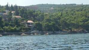A coastal town with buildings along the shoreline, a body of water in the foreground, and a hill with trees and structures in the background. - Apartment Sea Side - Two Bedroom Apartment with Sea View Terrace (ST) (Postira)