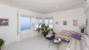 A bright living room with a large window, a sofa, a coffee table, and a potted plant. - Apartment Rea-Three Bedroom Apartment with Sea View (Dubrovnik)