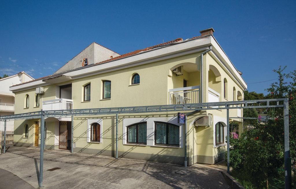 A two-story building with a balcony on the second floor, a covered entrance, and a small garden area.