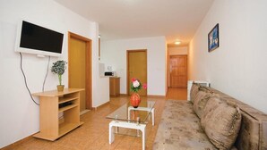 A living room with a TV, a coffee machine, a sofa, and a small table with a vase of flowers.