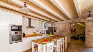A kitchen with white cabinets, a wooden countertop, and a stone wall. There is a dining table with chairs and a hanging light fixture. - Villa Kanada - Two-Bedroom House with Terrace and Sea View (Brsecine)