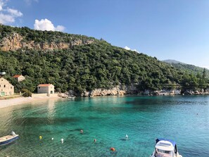 A coastal area with clear turquoise water, a small boat, and a building on the shore.