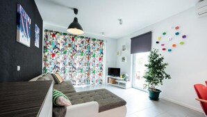 Un soggiorno moderno con un divano componibile, una TV a schermo piatto, una pianta in vaso e un'ornamento colorato al muro.