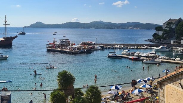 A coastal marina with boats, a dock, and people swimming and sunbathing.