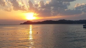 A sunset over a calm sea with a distant landmass and a boat.