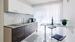 Une cuisine moderne dotée d’un plan de travail en marbre, d’une machine à café, d’un four à micro-ondes et d’une table en verre accompagnée de deux tabourets de bar.