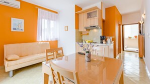 Ein modernes Wohnzimmer mit einer Couch, einem Esstisch und Stühlen. Es gibt eine Küche mit Schränken und einem Herd.