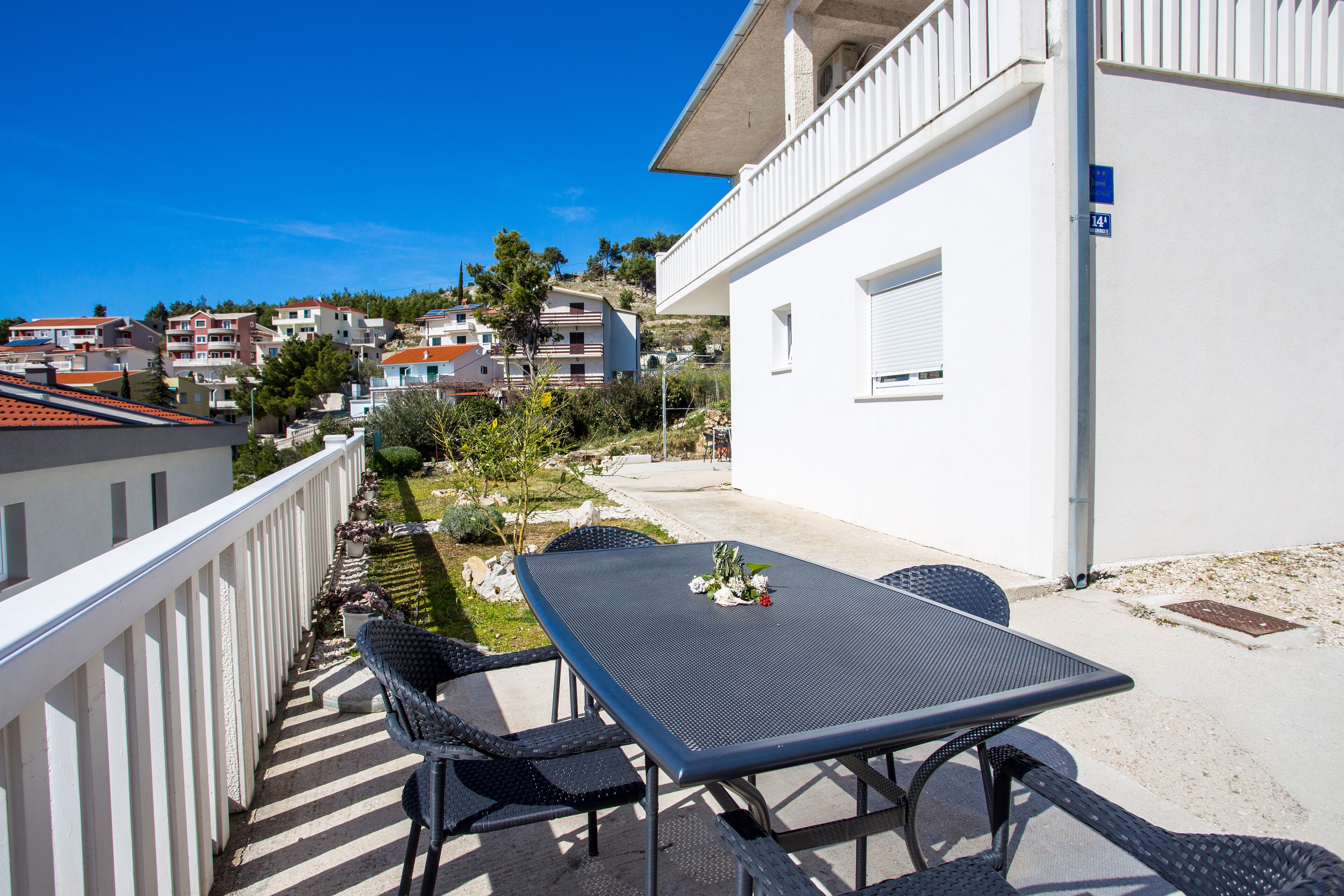 A balcony with a table and chairs, overlooking a residential area with houses and greenery.