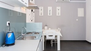A modern kitchen with a white countertop, stainless steel sink, and a blue kettle. There is a dining area with a white table and chairs. - Magdales - Two Bedroom Apartment with Balcony (Omis)